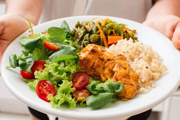 A plate of grilled chicken, brown rice, sautéed green beans and carrots, and a garden salad.